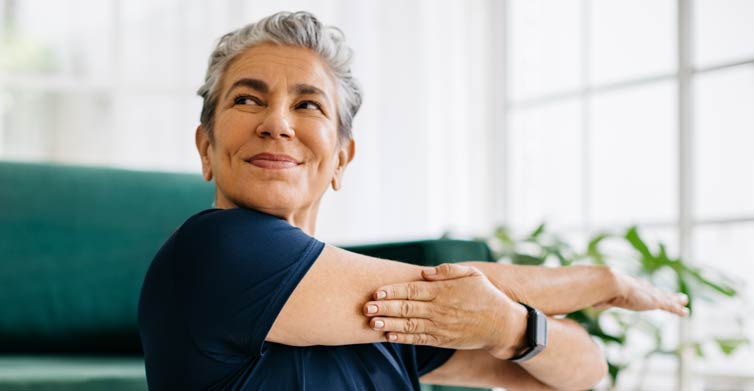 Gray-haired woman doing stretches in front of a couch.