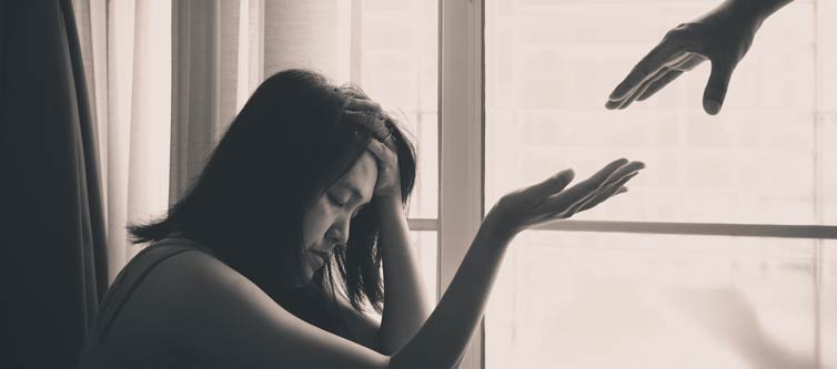 Black and white photo of young woman with her head in one hand and reaching outward toward an extended helping hand.