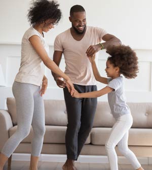 Mom, dad and young daughter holding hands and dancing in their living room.