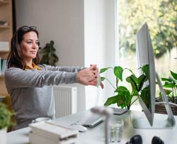 Young woman at desk doing reversal of posture exercise with her arms