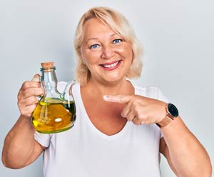 Smiling woman holding a flask of oil in one hand and pointing at it with the index finger of her other hand. 