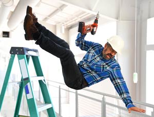 Man in hard hat holding a cordless drill falling off a ladder.