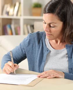 Women at desk completing a form with a stack of bills on the desk next to her.