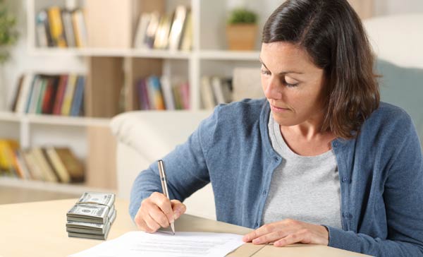 Women at desk completing a form with a stack of bills on the desk next to her.