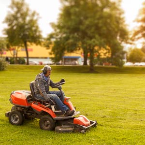 Man operating a tractor mower in an open, park setting.