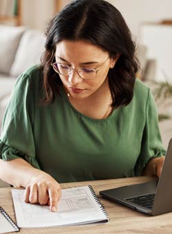 Woman comparing printed data to data on laptop screen.