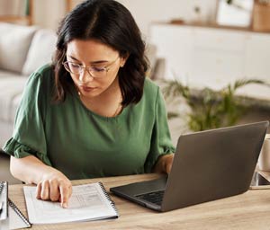 Woman comparing printed data to data on laptop screen.